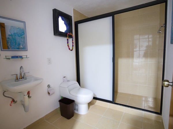 Baño completo con lavabo empotrado, inodoro y amplia regadera con puerta de vidrio esmerilado