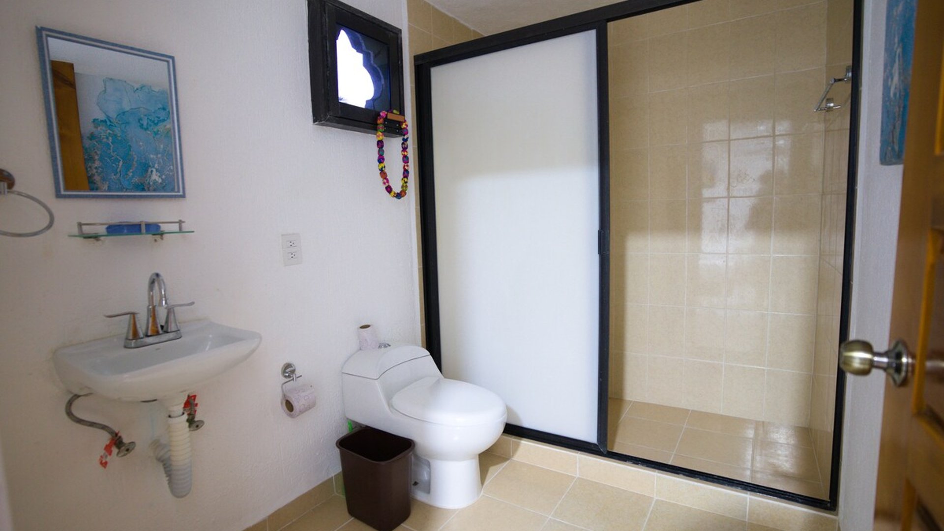 Baño completo con lavabo empotrado, inodoro y amplia regadera con puerta de vidrio esmerilado
