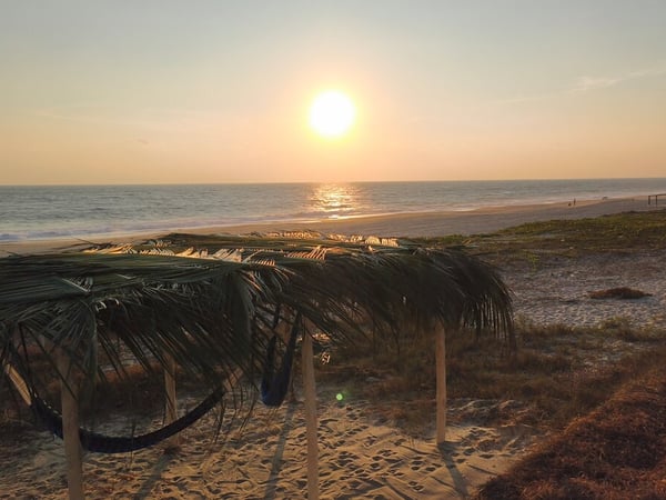 Palapa rústica con hamaca frente al mar en la playa al atardecer dorado