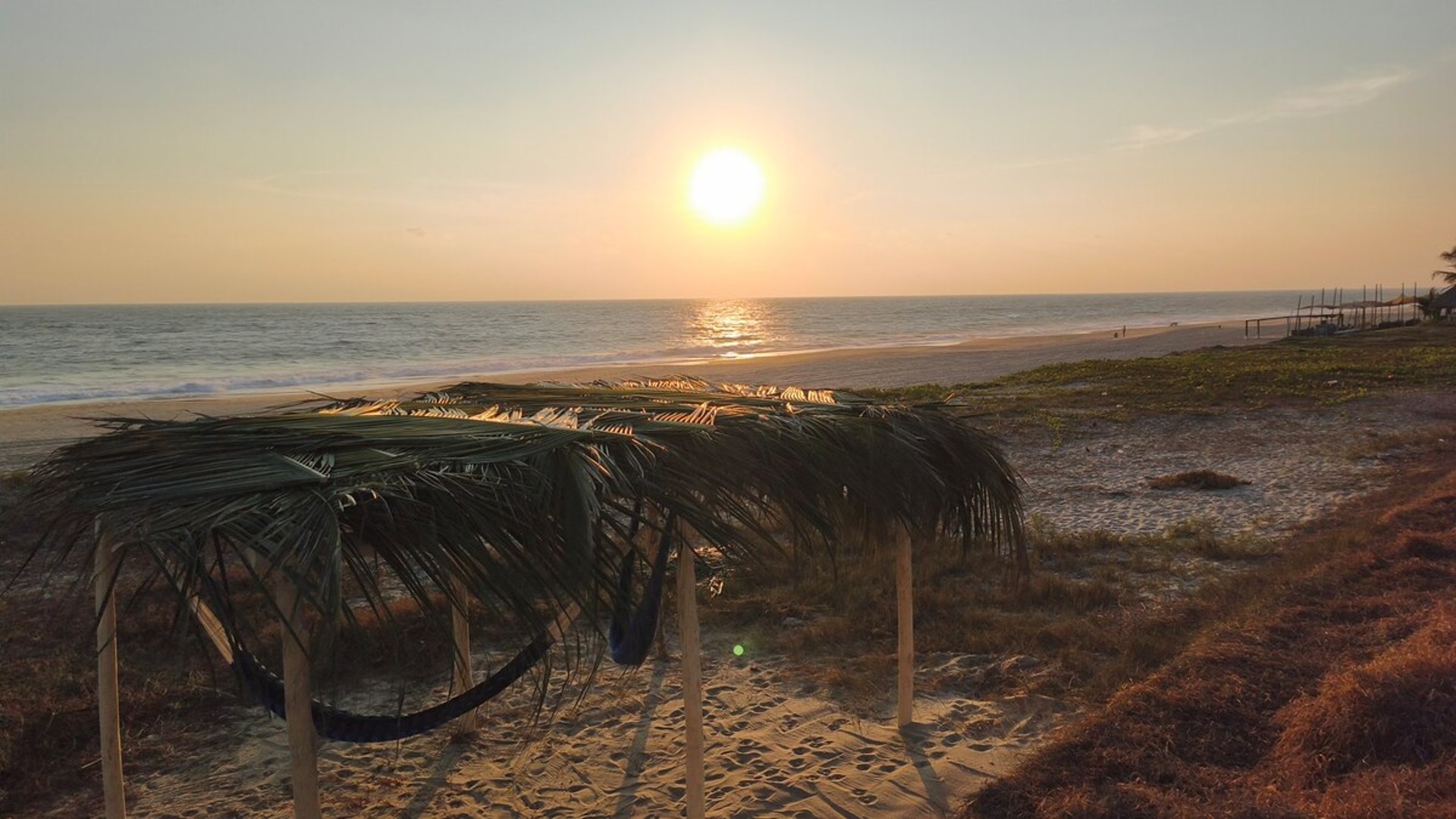 Palapa rústica con hamaca frente al mar en la playa al atardecer dorado