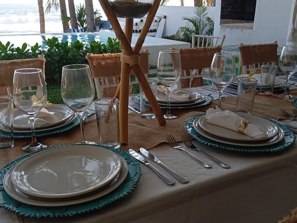 Mesa de banquete montada con vajilla elegante y vista al mar y alberca al fondo