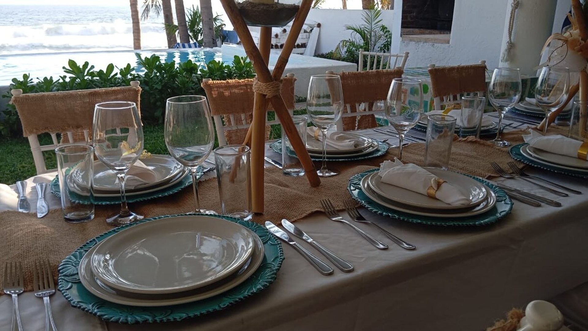 Mesa de banquete montada con vajilla elegante y vista al mar y alberca al fondo