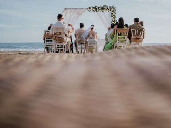 Ceremonia de boda en playa con arco floral y cortinas blancas frente al mar con invitados