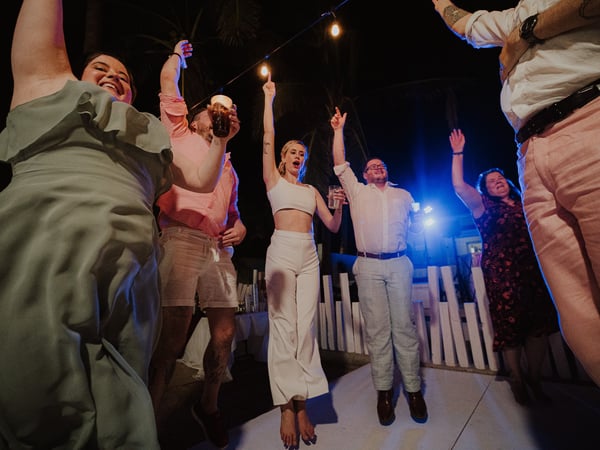 Invitados celebrando en pista de baile nocturna con luces colgantes y palmeras de fondo