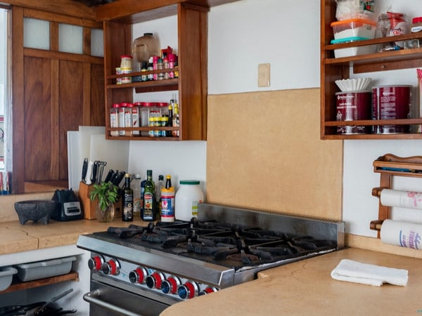 Cocina equipada con estufa de gas industrial, gabinetes de madera y repisas con especias y utensilios de cocina