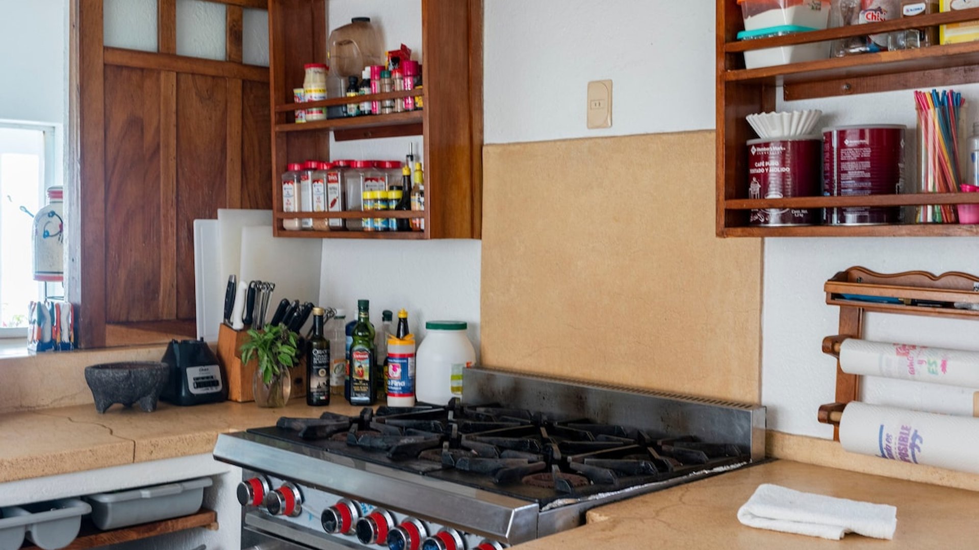 Cocina equipada con estufa de gas industrial, gabinetes de madera y repisas con especias y utensilios de cocina