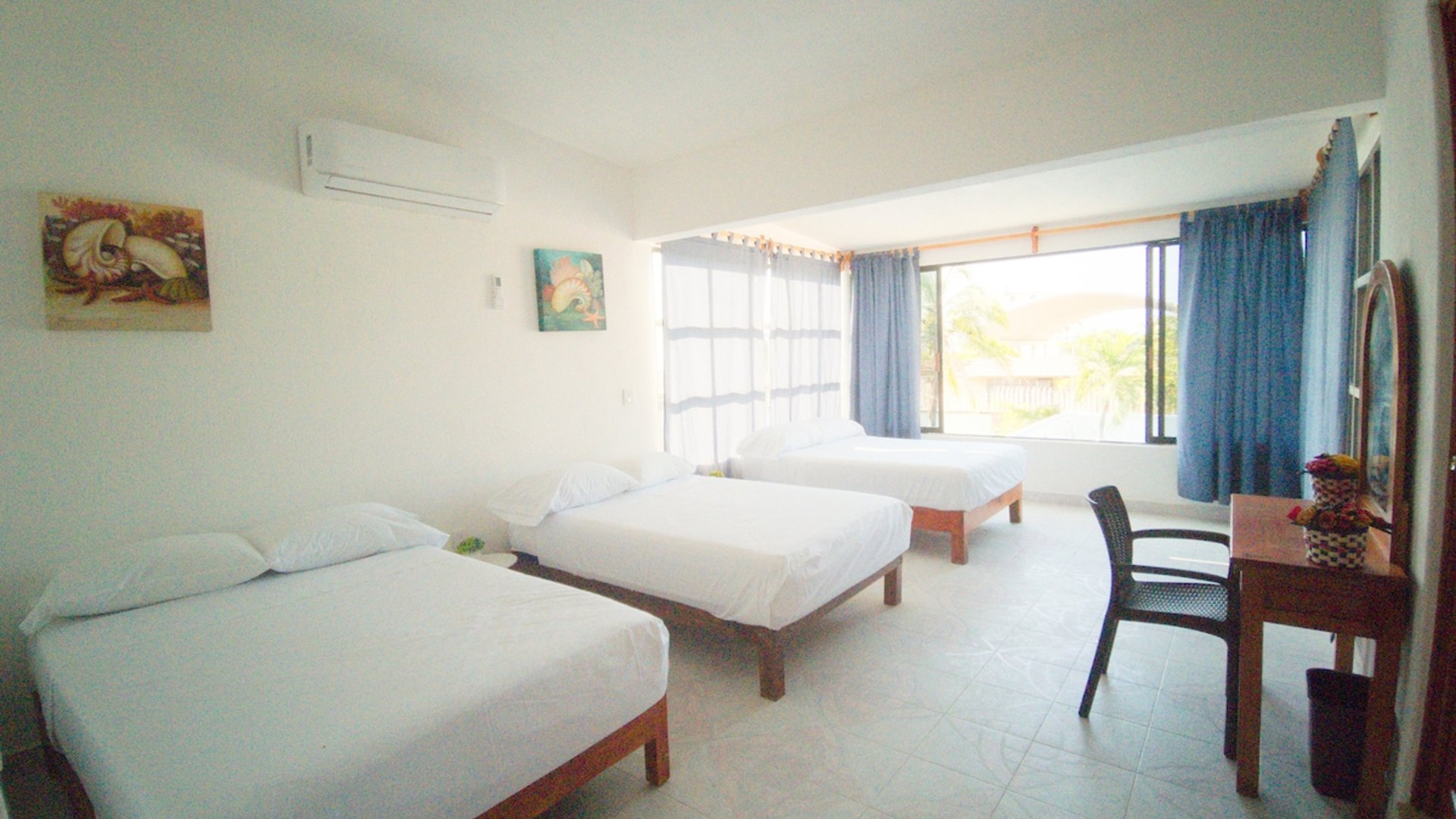 Recámara amplia con tres camas individuales, ropa de cama blanca, aire acondicionado y ventanas con cortinas azules