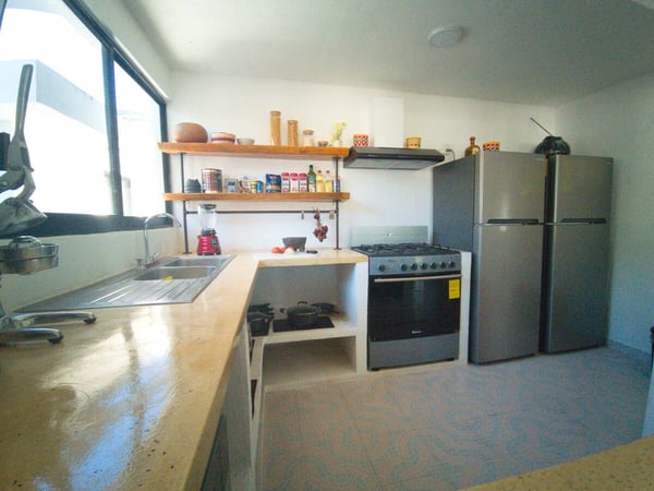 Cocina equipada con estufa de gas, refrigerador, fregadero y repisas de madera con especias y utensilios