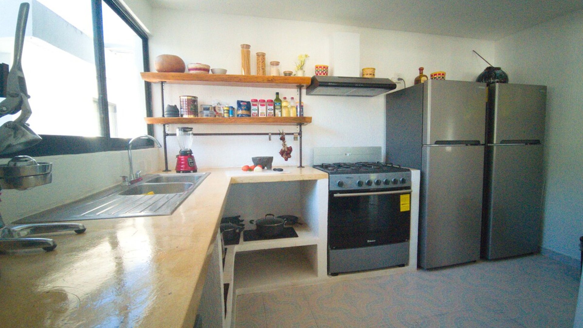 Cocina equipada con estufa de gas, refrigerador, fregadero y repisas de madera con especias y utensilios