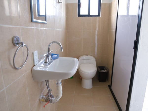 Baño completo con azulejo beige, lavabo empotrado, inodoro y cabina de ducha con marco negro