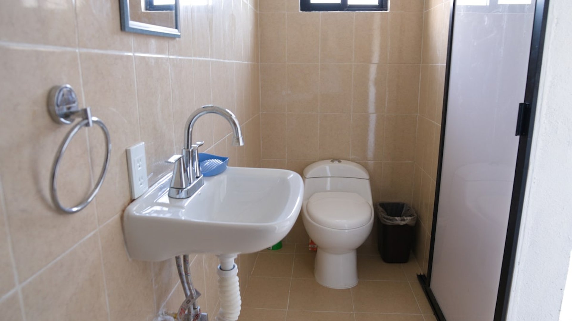 Baño completo con azulejo beige, lavabo empotrado, inodoro y cabina de ducha con marco negro