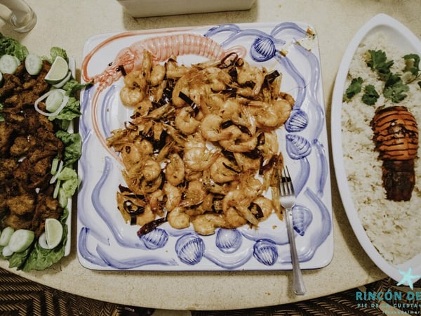 Platillos de mariscos servidos en mesa: camarones al ajillo, botana frita con ensalada y arroz con langosta
