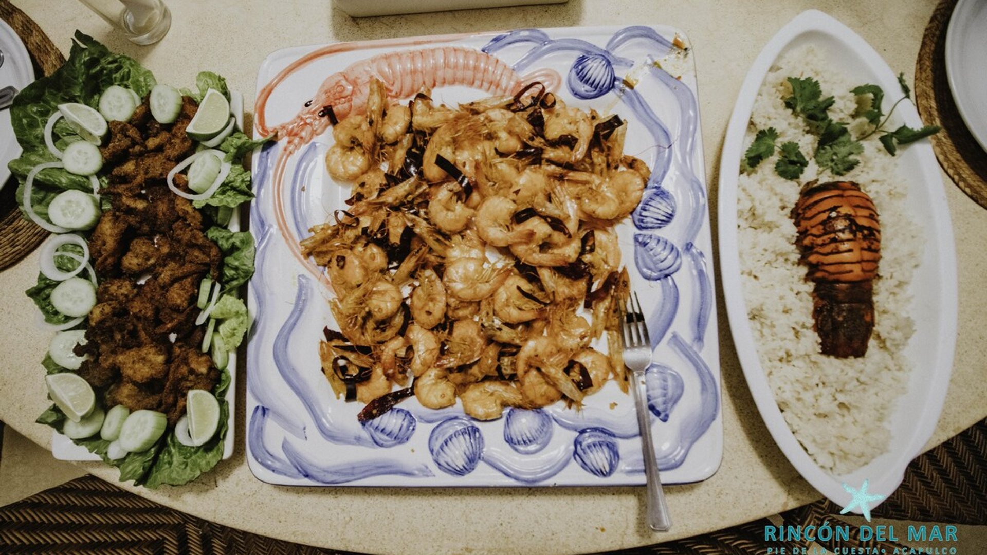 Platillos de mariscos servidos en mesa: camarones al ajillo, botana frita con ensalada y arroz con langosta