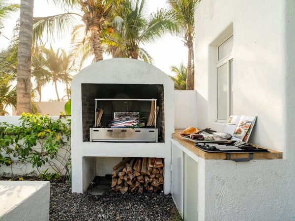 Asador de leña exterior con pescados frescos listos para cocinar, rodeado de palmeras a la luz del atardecer