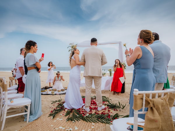 Ceremonia de boda en playa con arco blanco, pasillo de pétalos y sillas frente al Pacífico