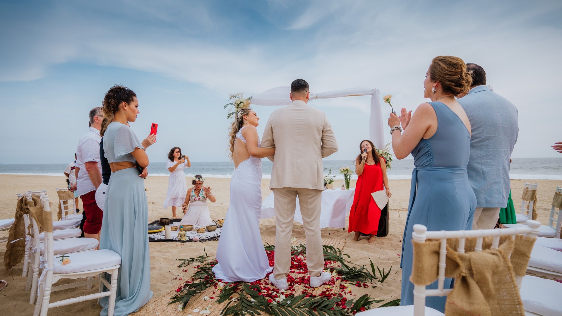 Ceremonia de boda en playa con arco blanco, pasillo de pétalos y sillas frente al Pacífico