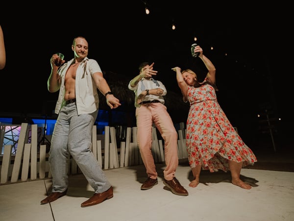 Invitados bailando en terraza nocturna frente a alberca iluminada con ambiente festivo de boda