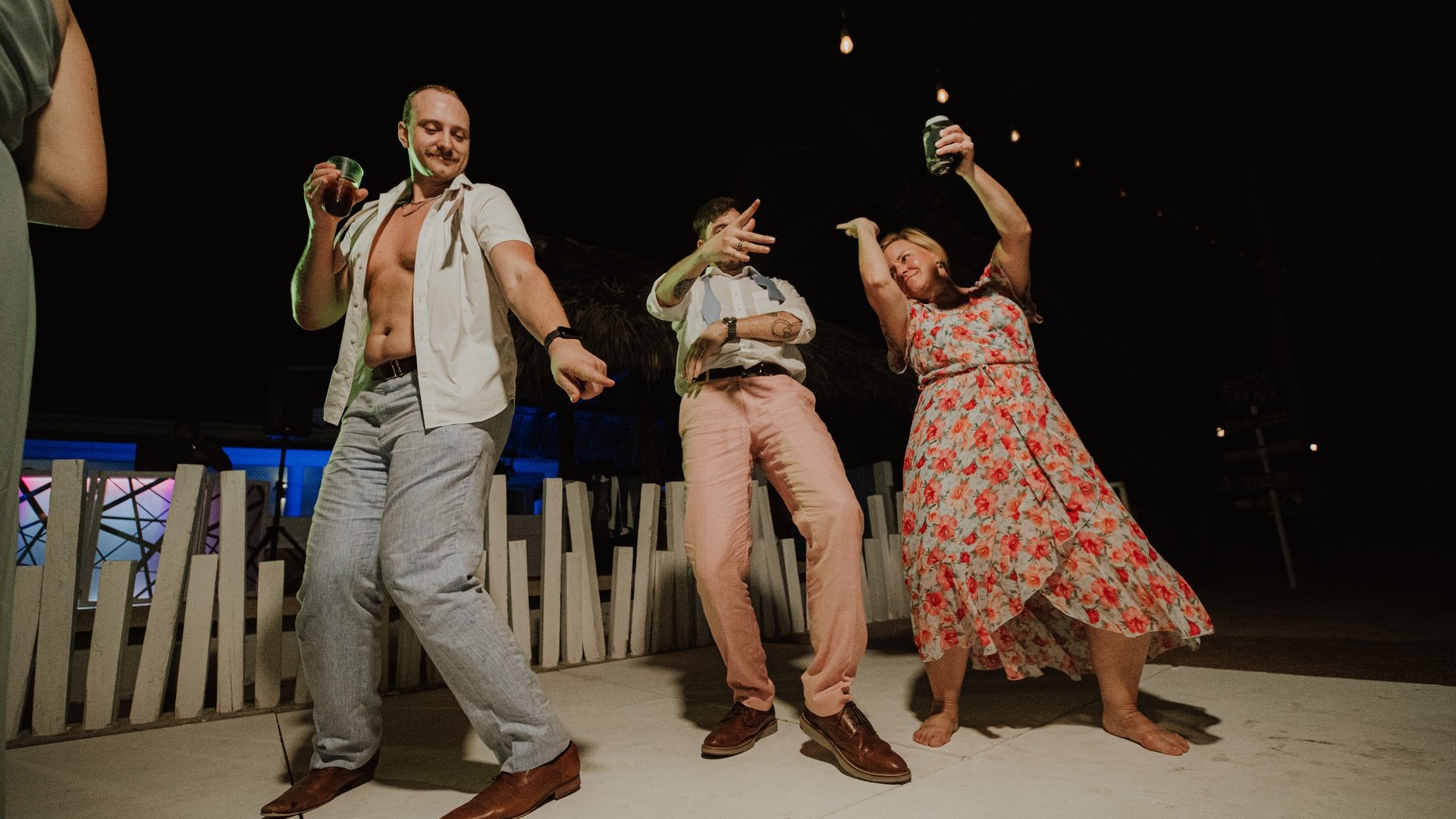 Invitados bailando en terraza nocturna frente a alberca iluminada con ambiente festivo de boda