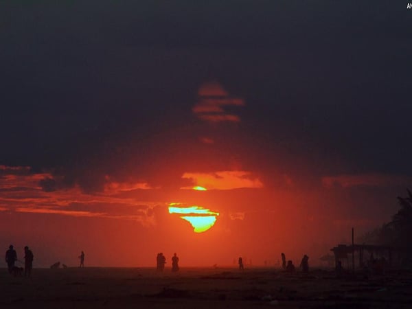 Atardecer dramático en la playa con siluetas de personas y sol entre nubes rojas