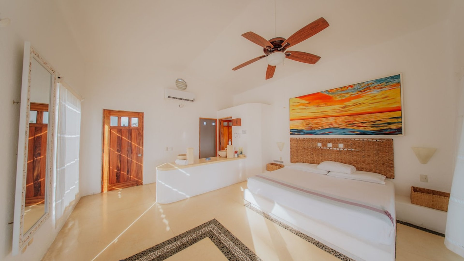 Recámara amplia con cama doble, cabecera de mimbre, cuadro de atardecer y techo alto con ventilador