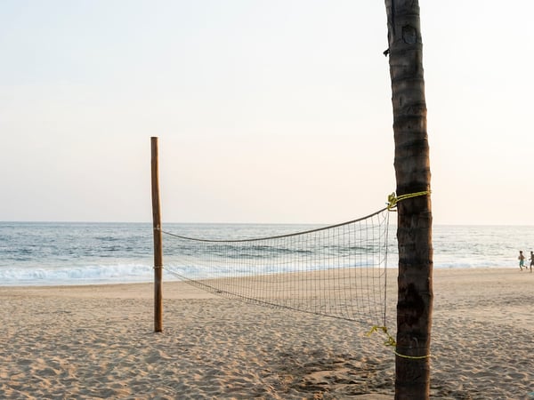 Red de voleibol playero frente al mar en tarde dorada, personas al fondo en la orilla