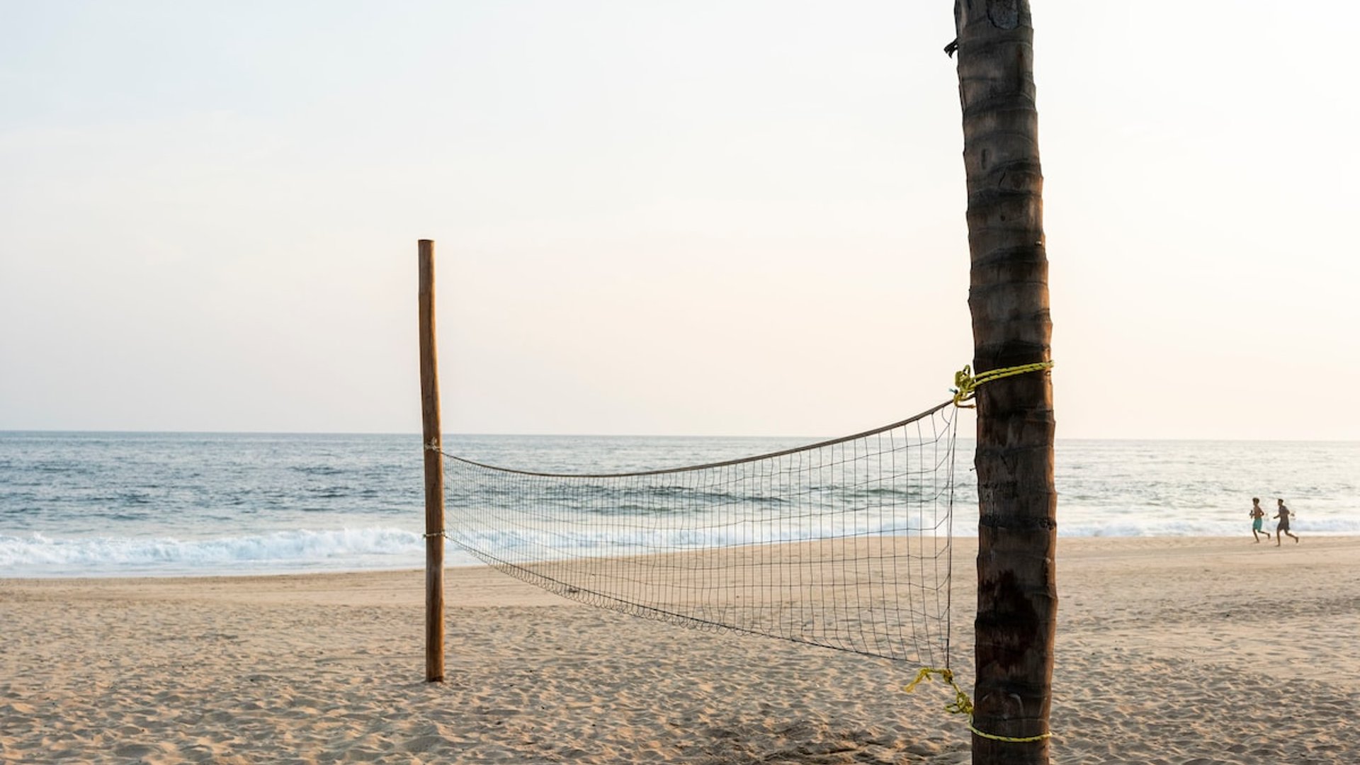 Red de voleibol playero frente al mar en tarde dorada, personas al fondo en la orilla