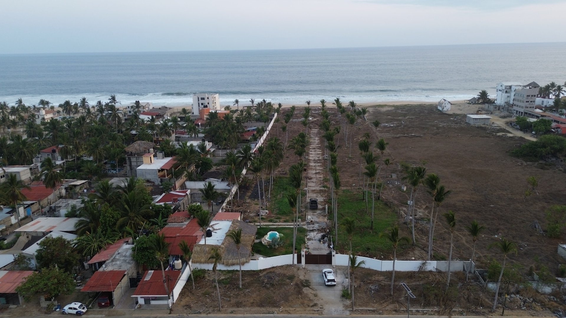 Vista aérea de propiedad frente al mar con palmeras alineadas, alberca y acceso vehicular en Pie de la Cuesta
