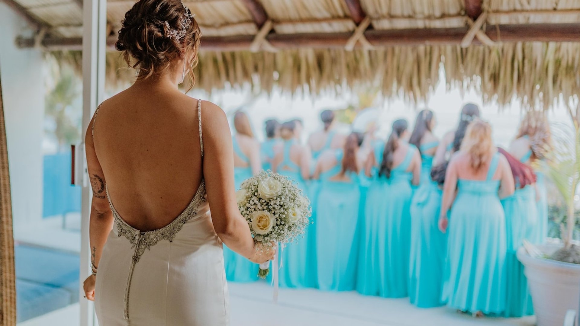 Novia con ramo de rosas blancas bajo palapa frente a damas de honor en vestidos turquesa