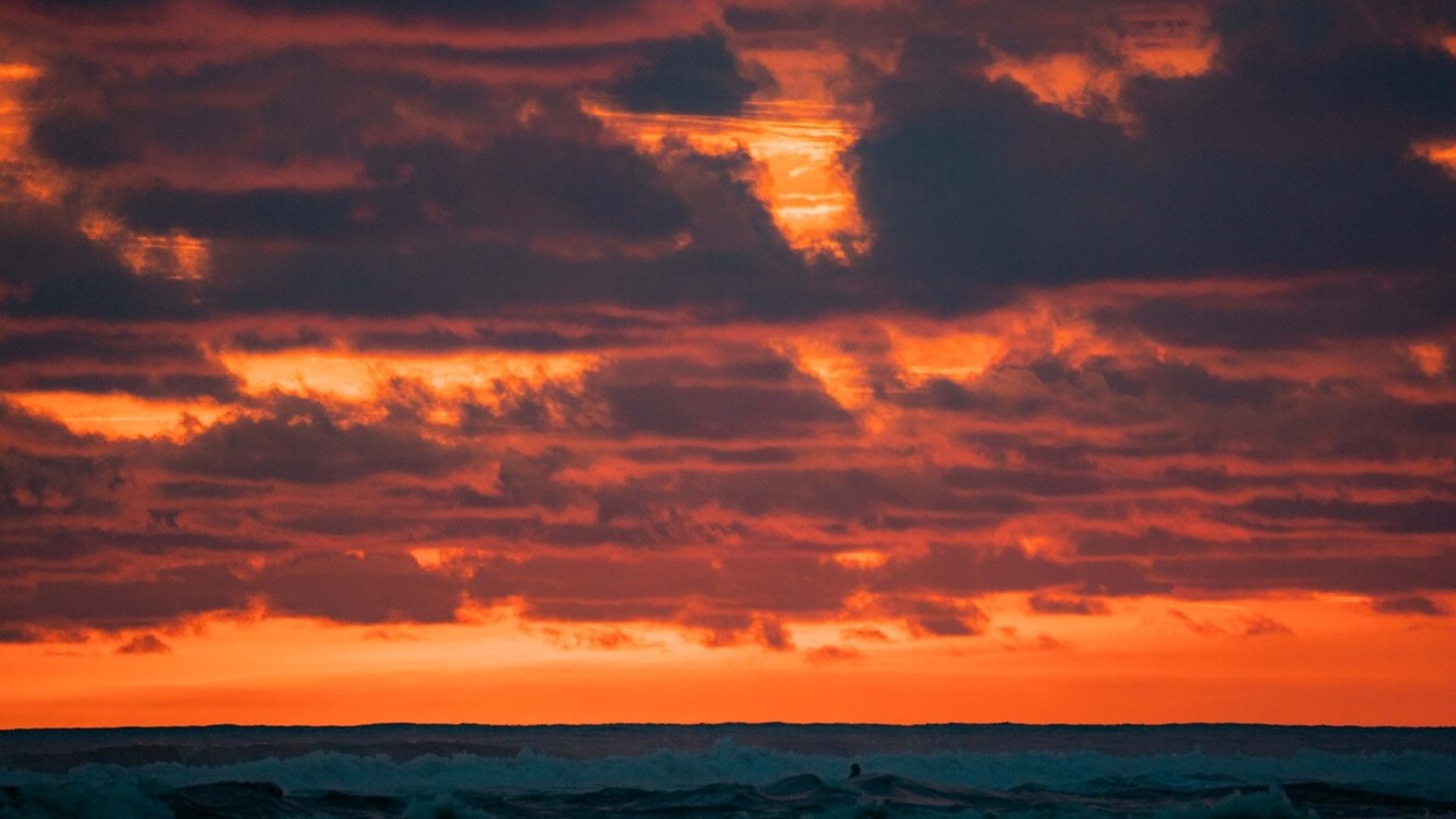 Atardecer intenso sobre el mar con cielo en llamas de tonos naranja y nubes dramáticas