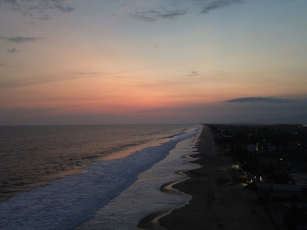 Vista aérea de la línea costera al atardecer con cielo en tonos rosados y mar tranquilo