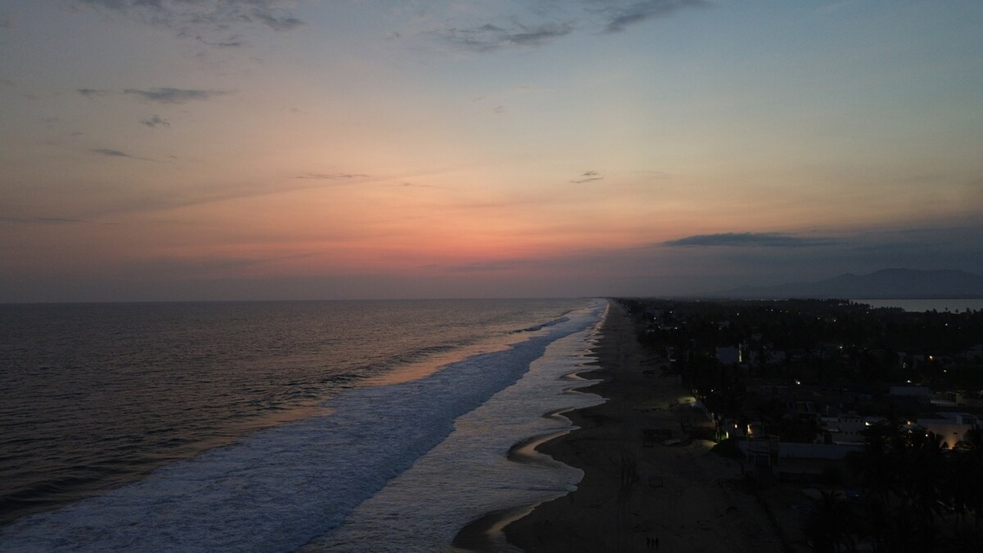 Vista aérea de la línea costera al atardecer con cielo en tonos rosados y mar tranquilo