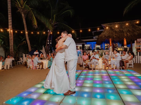 Primer baile nocturno en pista iluminada con luces de colores bajo palmeras y guirnaldas de focos