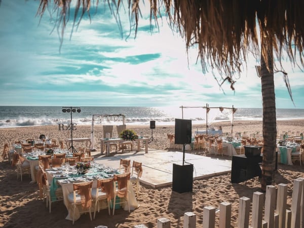 Montaje de boda en la playa con mesas decoradas en menta y dorado, pista de baile y el mar de fondo