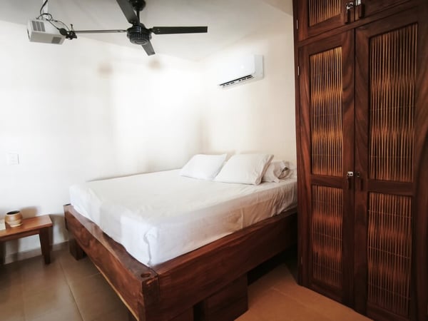 Recámara con cama matrimonial en madera, armario de madera oscura, aire acondicionado y ventilador de techo
