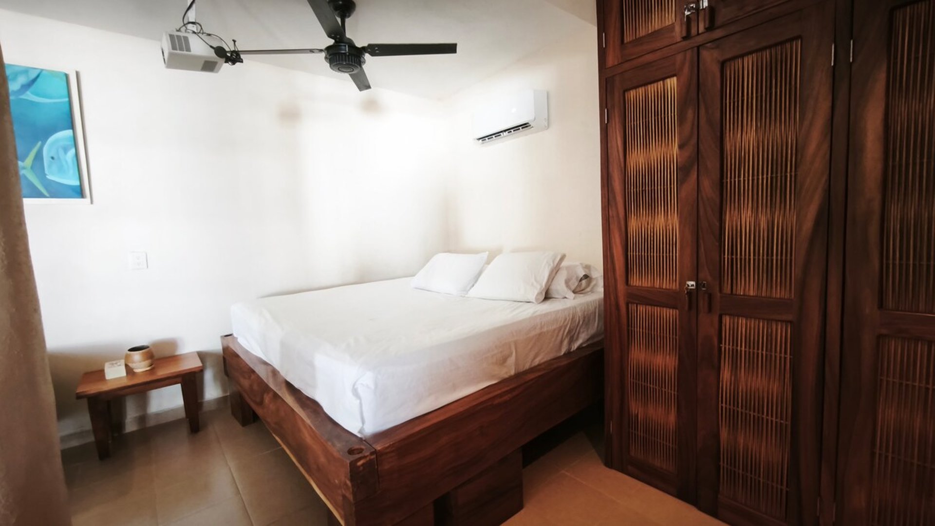 Recámara con cama matrimonial en madera, armario de madera oscura, aire acondicionado y ventilador de techo