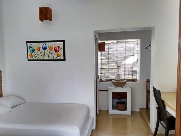 Recámara sencilla con paredes blancas, cuadro de tulipanes, cama doble y área de lavabo con ventana de bambú