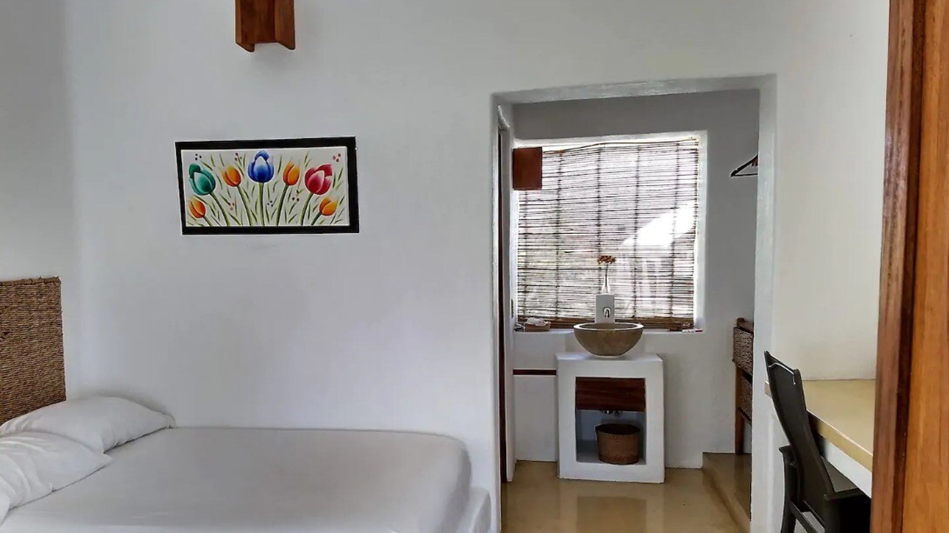 Recámara sencilla con paredes blancas, cuadro de tulipanes, cama doble y área de lavabo con ventana de bambú