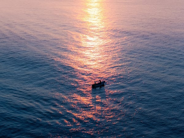 Pequeña lancha en el Pacífico al atardecer, con reflejo dorado del sol sobre el mar en calma