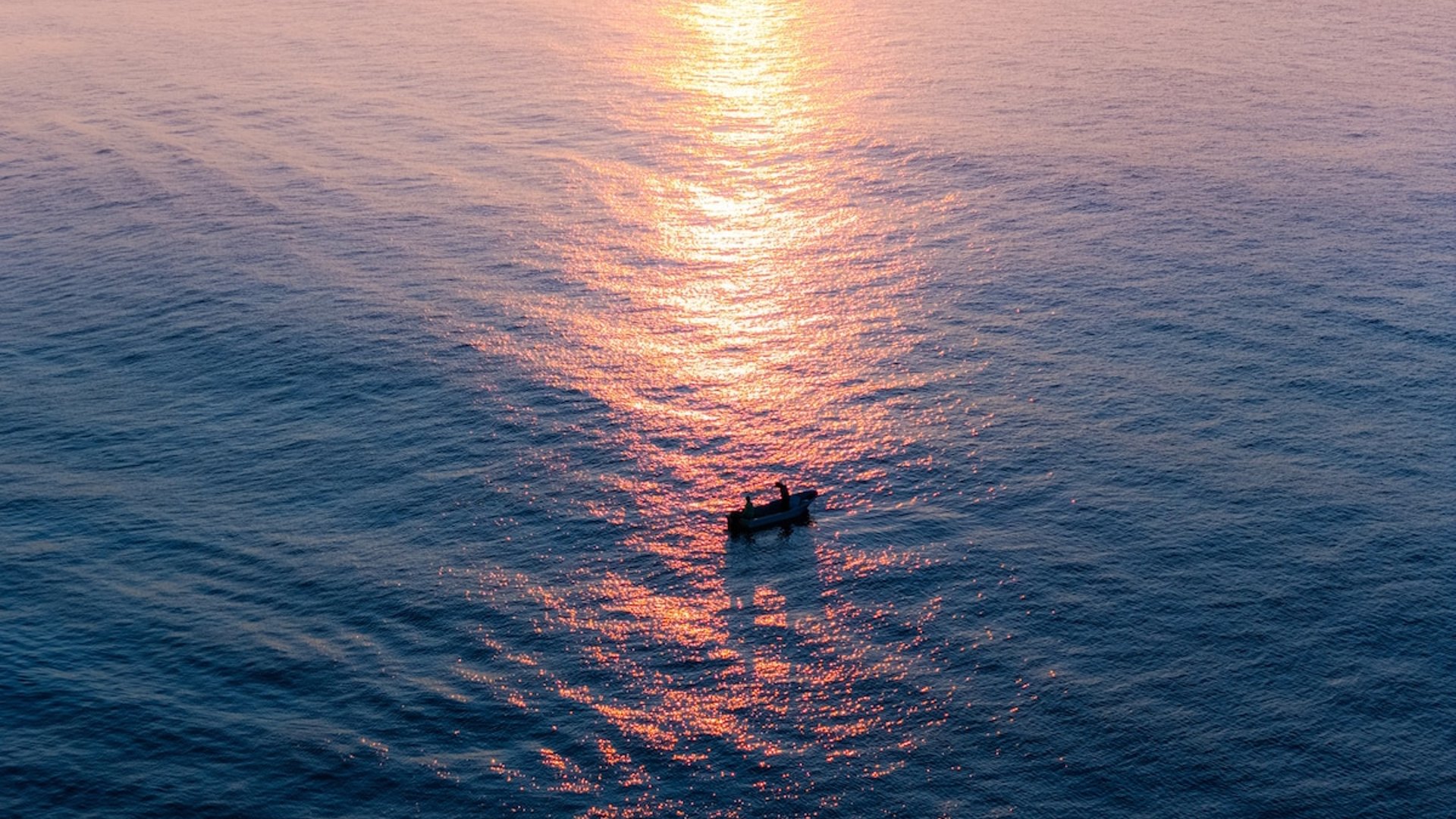 Pequeña lancha en el Pacífico al atardecer, con reflejo dorado del sol sobre el mar en calma