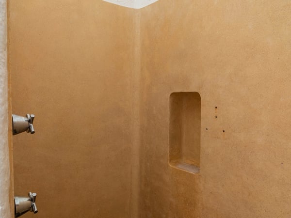 Interior de regadera con paredes de cemento pulido color ocre, nicho empotrado y llaves de cruz en acero