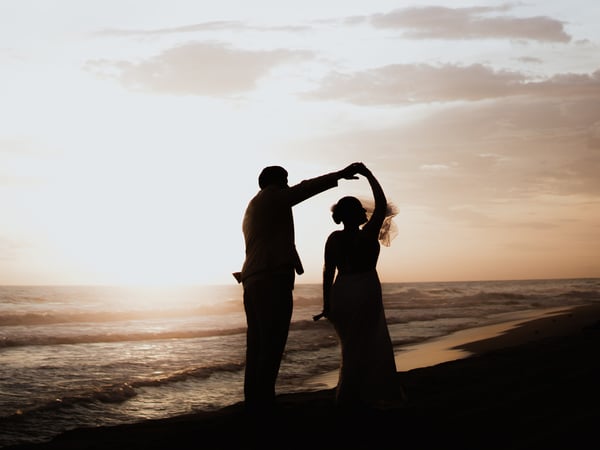 Silueta de pareja bailando en playa del Pacífico al atardecer con olas doradas