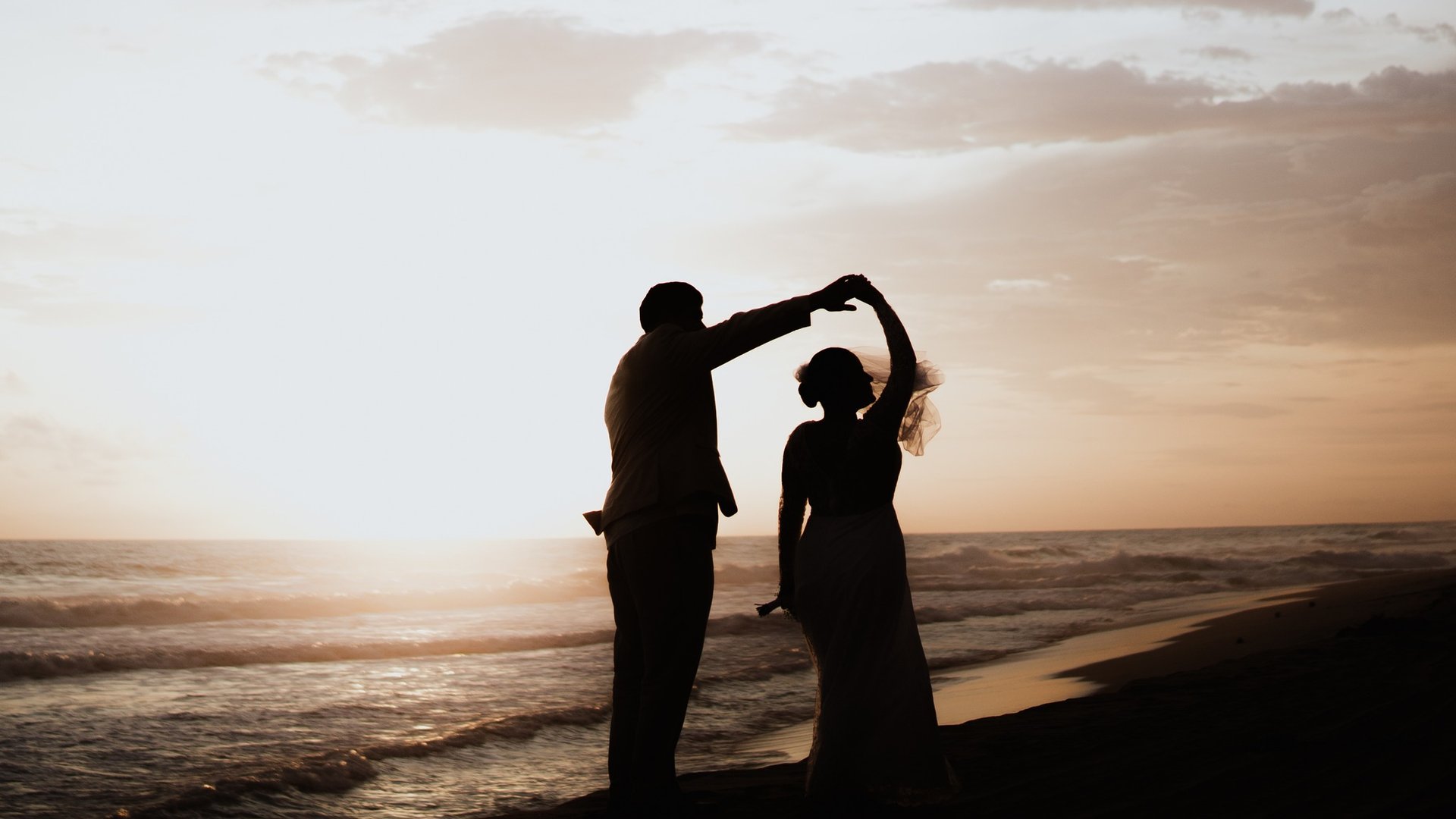 Silueta de pareja bailando en playa del Pacífico al atardecer con olas doradas
