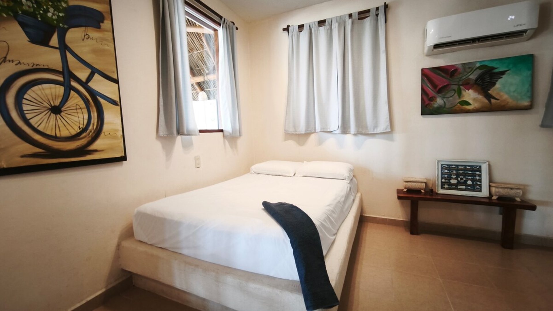 Recámara sencilla con cama doble en ropa blanca, pinturas coloridas en paredes y aire acondicionado mini-split