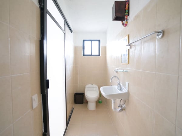 Baño compacto con azulejo beige, lavabo empotrado, inodoro y ventana al fondo