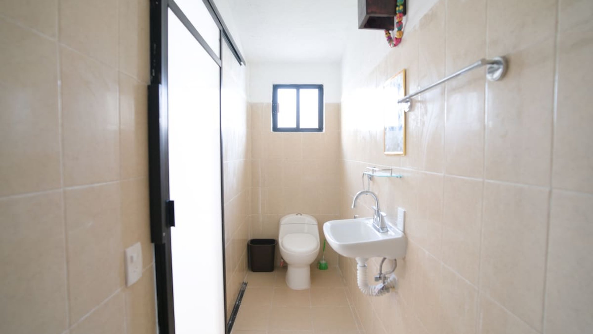 Baño compacto con azulejo beige, lavabo empotrado, inodoro y ventana al fondo