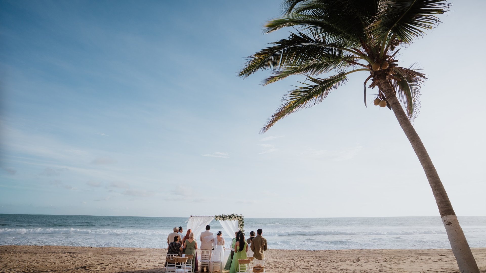 Ceremonia de boda íntima en playa con arco floral blanco y palmera frente al Pacífico