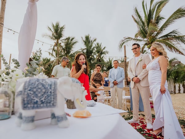 Ceremonia de boda en playa con sillas blancas, palmeras tropicales y telas decorativas al aire libre