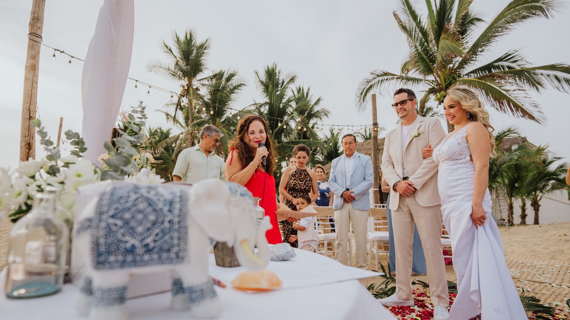 Ceremonia de boda en playa con sillas blancas, palmeras tropicales y telas decorativas al aire libre