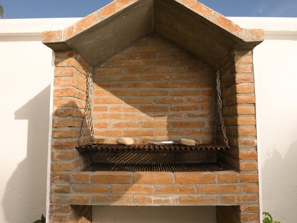 Asador de ladrillo con parrilla ajustable por cadenas, construido en muro exterior bajo cielo despejado