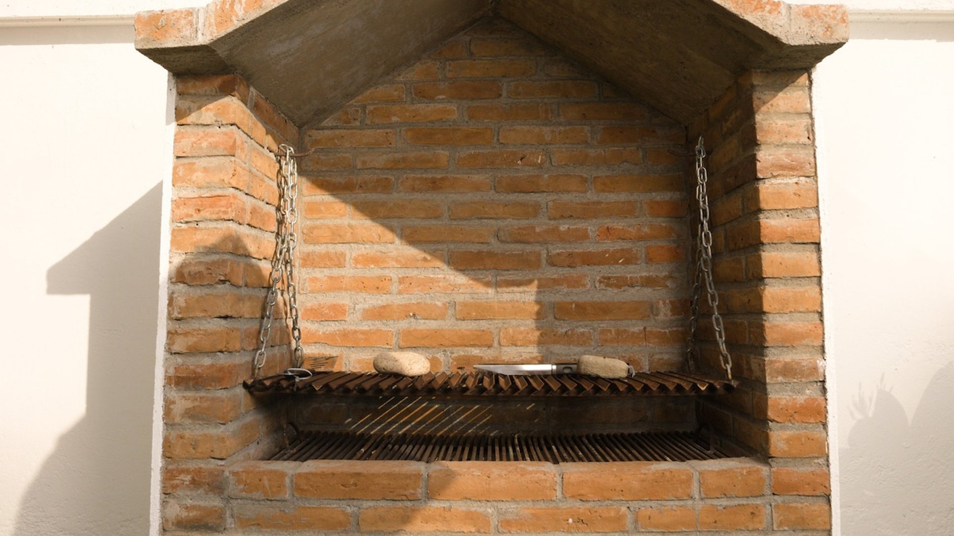 Asador de ladrillo con parrilla ajustable por cadenas, construido en muro exterior bajo cielo despejado